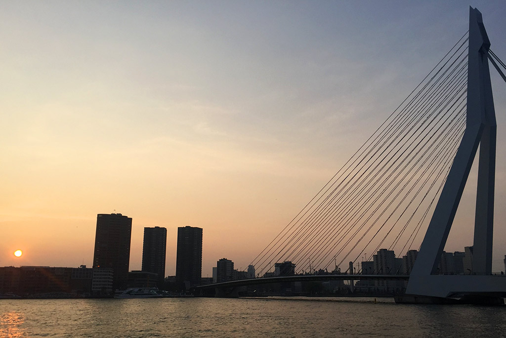 a modern bridge over water by a city silhouetted at sunset