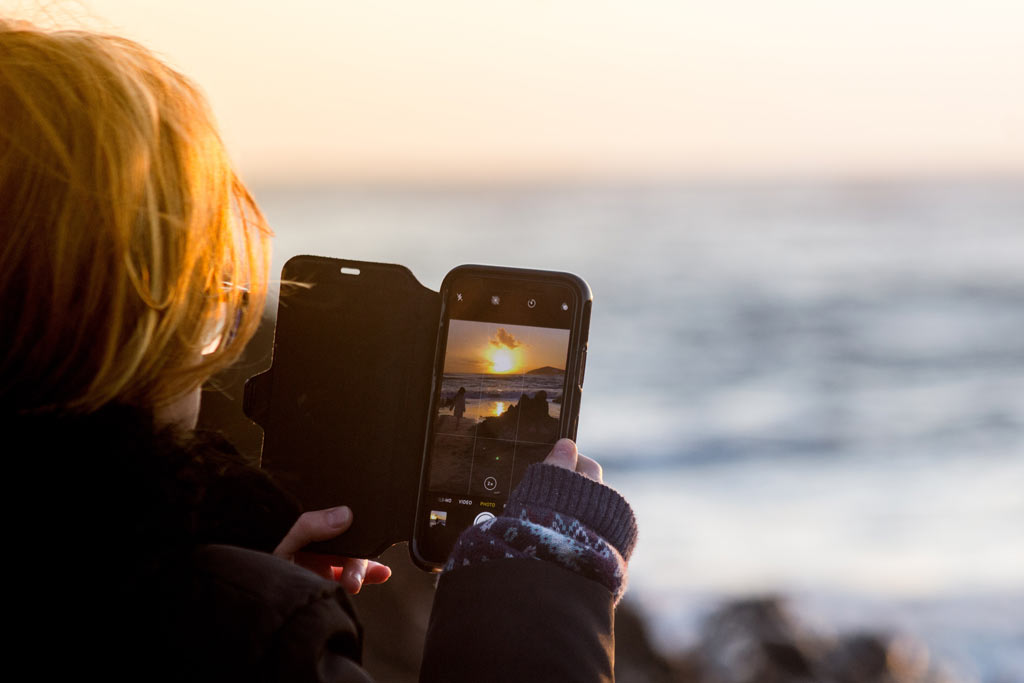 Person along a shoreline viewing the ocean on their smartphone screen