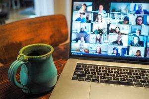 Laptop displaying a Zoom meeting next to handcrafted coffee mug on a desk